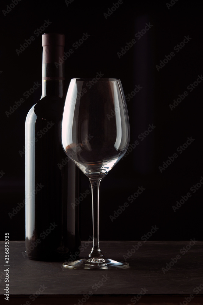 A bottle of red wine with a beautiful wine glass on a dark background A bottle of red wine with a beautiful wine glass on a dark background