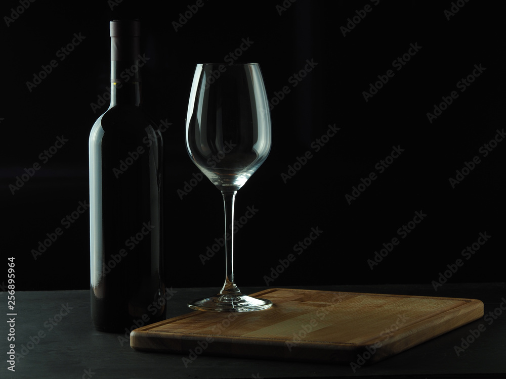 A bottle of red wine with a beautiful wine glass on a dark background A bottle of red wine with a beautiful wine glass on a dark background