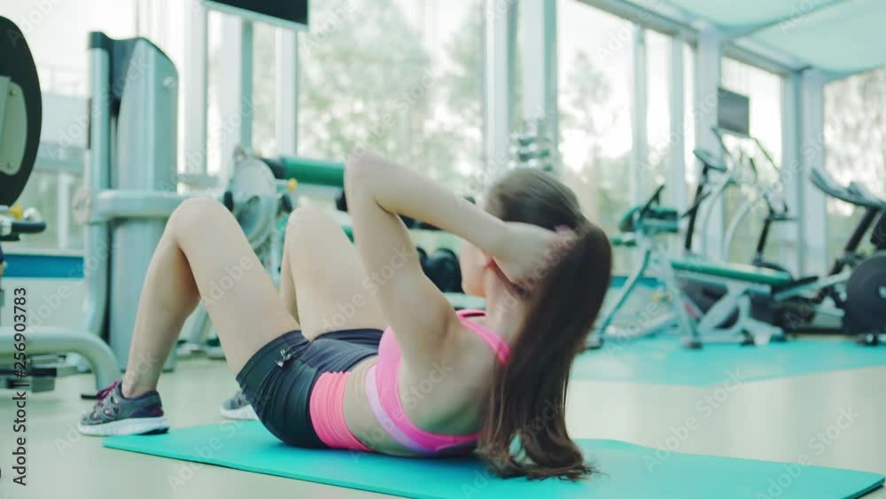 Side view of determined fit woman lying on exercise mat in gym and doing abdominal crunches Side view of determined fit woman lying on exercise mat in gym and doing abdominal crunches