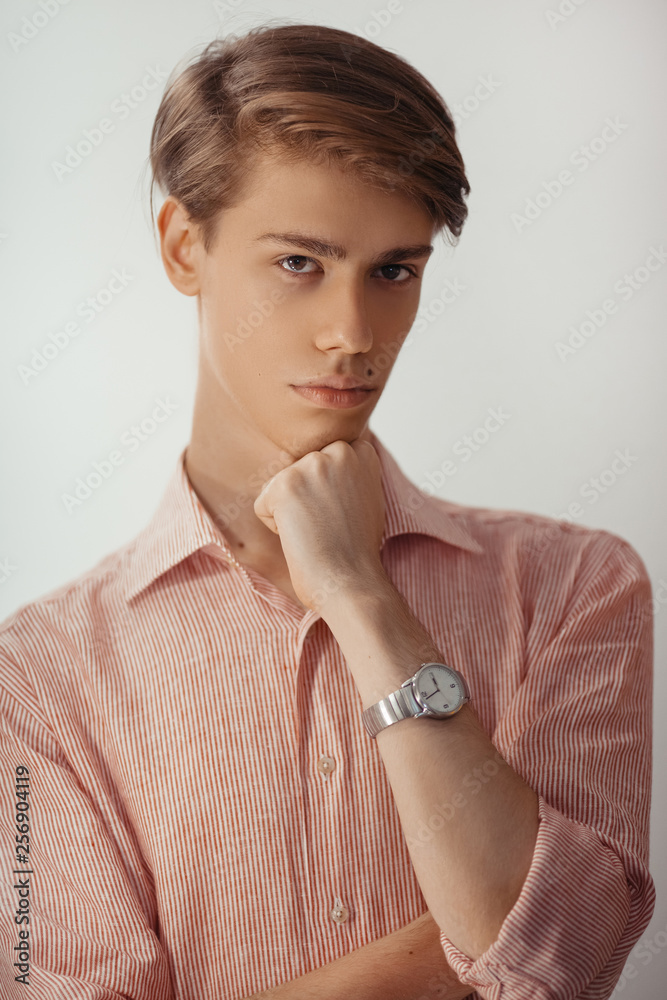I have some doubt. Handsome young man looking at camera indoor and keeping hand on chin while standing against blank background I have some doubt. Handsome young man looking at camera indoor and keeping hand on chin while standing against blank background