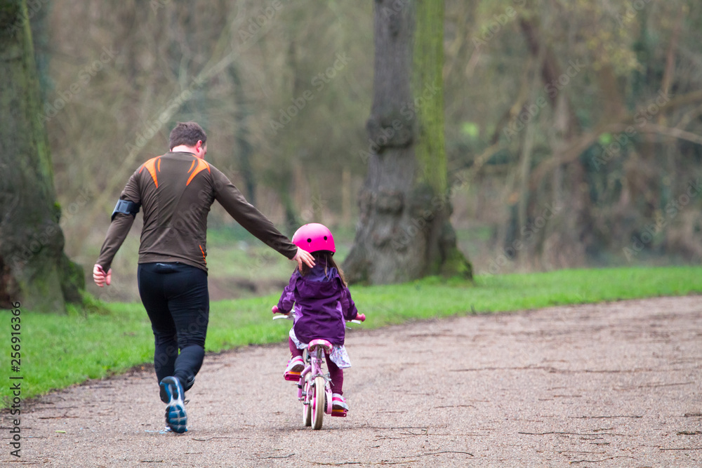 Fototapeta premium A father runs alongside his daughter who is learning to ride a bike in Shrewsbury, Shropshire, England.