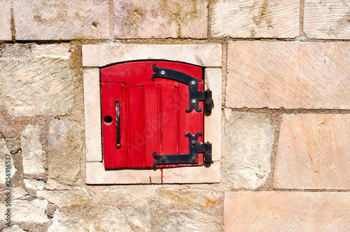 One small arched red door with metal higes on a stone wall photo