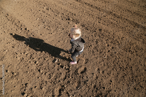 Cute baby girl playing with dirt on the flat plot agricultural land