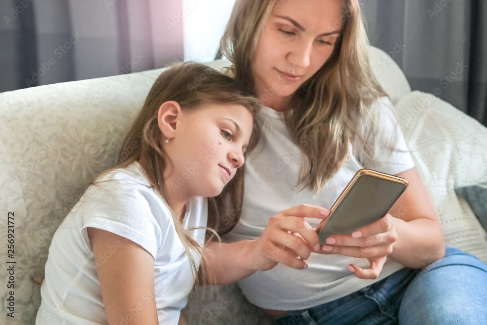 mom and daughter are sitting on the couch at home with the phone mom and daughter are sitting on the couch at home with the phone