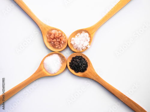 Wooden spoons with himalayan salt, black hawaii salt, common salt and salt flakes on a white background