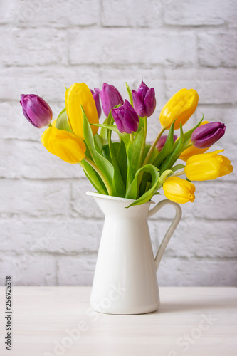 Yellow and purple live tulips in a white jug on a light background