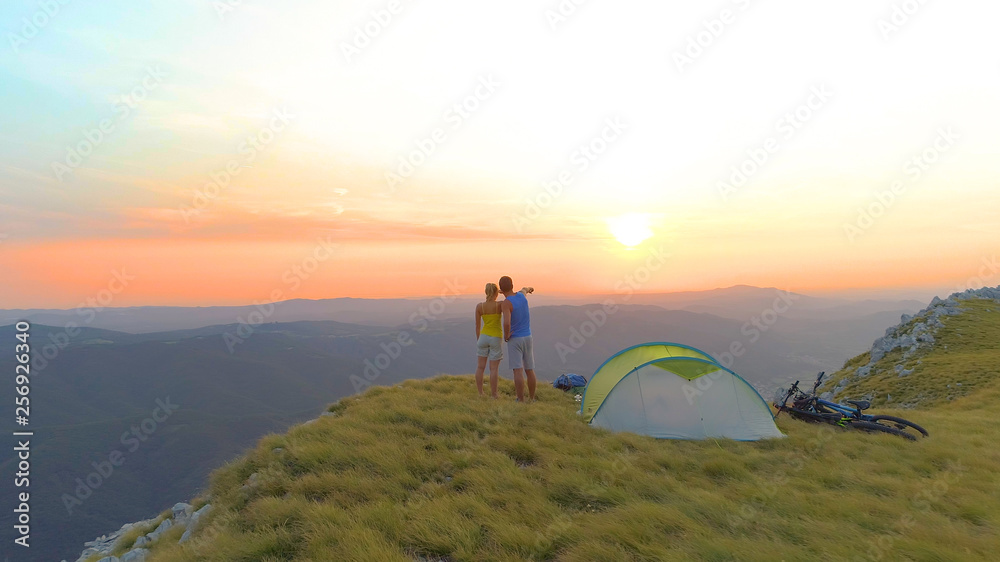 AERIAL: Unrecognizable woman and man observing the stunning mountains at sunrise