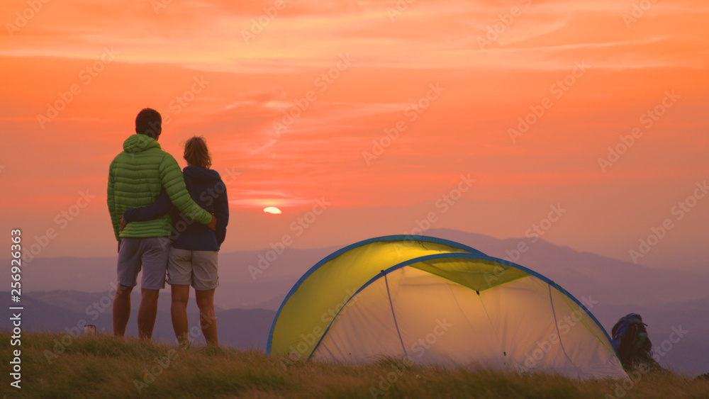COPY SPACE: Hiker couple stands embraced next to tent and watch the sunrise.