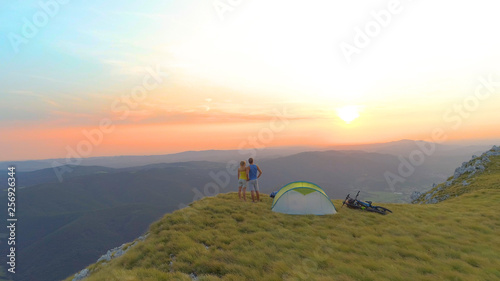 AERIAL: Flying behind unrecognizable male and female campers watching the sunset