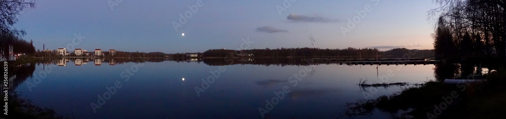 Beautiful lake scene panorama at night. Calm water and the moon on the clear sky. Beautiful lake scene panorama at night. Calm water and the moon on the clear sky.