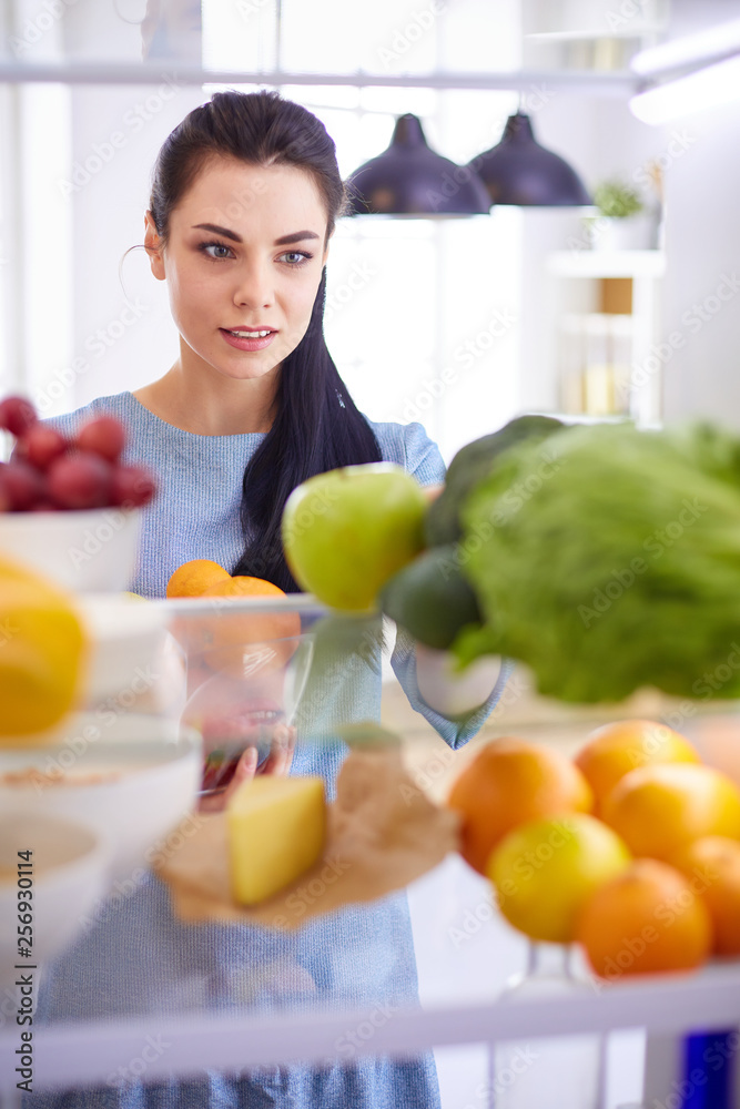 Smiling woman taking a fresh fruit out of the fridge, healthy food concept Smiling woman taking a fresh fruit out of the fridge, healthy food concept