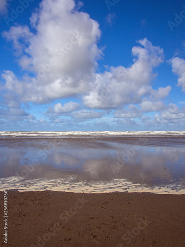 beautiful huge fluffy clouds and blue sky at Westward Ho in Devon reflecting in the wet sand on the beach