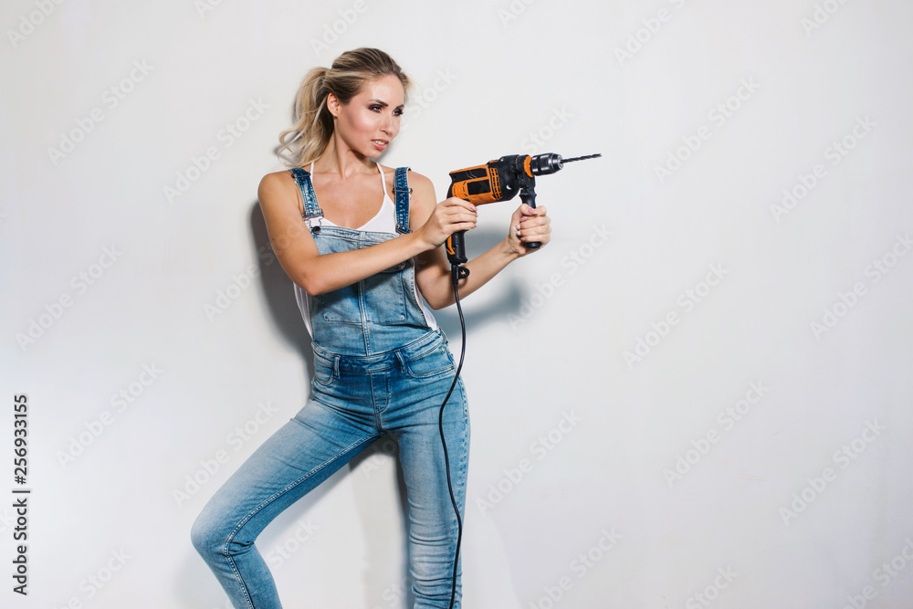Portrait of young woman worker at construction site with orange drill and construction tools. Sexy girl using a drill as a gun. Smiling and funny. Flat or house renovation concept Portrait of young woman worker at construction site with orange drill and construction tools. Sexy girl using a drill as a gun. Smiling and funny. Flat or house renovation concept
