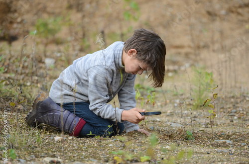 a boy in nature sitting on the ground looking at a magnifying glass plants
