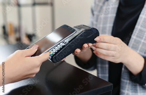 Close up of woman making wireless or contactless payment using her mobile phone. Cashier accepting payment over nfc technology