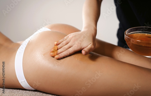 Beautiful young woman in spa salon having anti cellulite massage therapy with honey for fat burning. Honey massage concept at white background