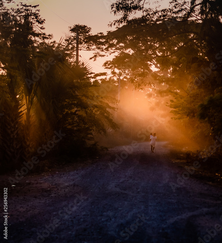 woman walking with child at sunset on dirt road in Guatemalan village