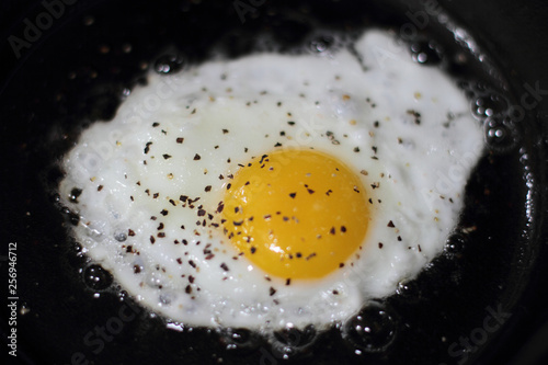 Egg sunny side up frying in a pan on the stove.