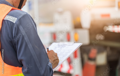 Fotografie, Obraz Preforming a pre-trip inspection on a truck,Concept preventive maintenance truck checklist,Truck driver holding clipboard with checking of truck,spot focus