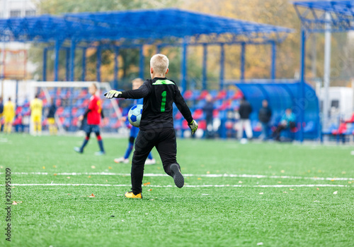 Goalkeeper kicks ball. Young footballers dribble and kick football ball in game. Boys in red blue sportswear running on soccer field. Training, active lifestyle, sport, children activity concept