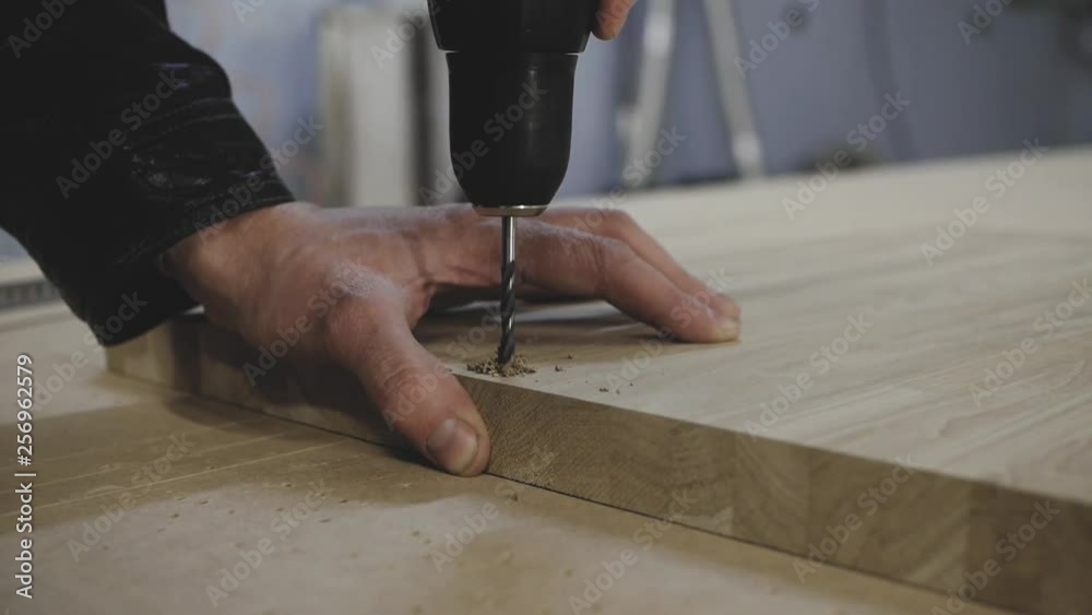 A man drills a hole in a wooden billet A man drills a hole in a wooden billet