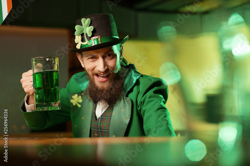 Fotografi Dark-haired bearded young man in a leprechaun hat with shamrock looking funny