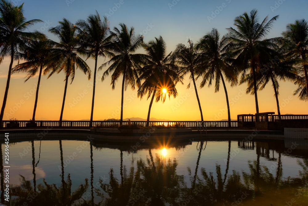 Warm tone, Swimming pool with Silhouette coconut tree and sea background, reflection of coconut trees on the swimming pool at the beach, Sunset  in Tropical island at Andaman sea, Ranong estuary,Thai