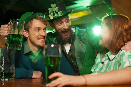 Red-haired pretty girl in a green checkered shirt and men in st.patricks day costumes celebrating together