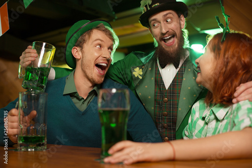 Red-haired pretty girl in a green checkered shirt and men in st,patricks day costumes laughing together