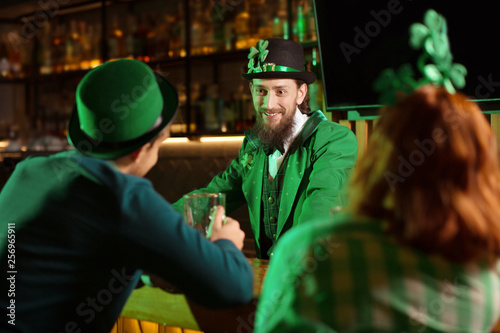 Dark-haired bearded young man in a leprechaun hat smiling to his friends