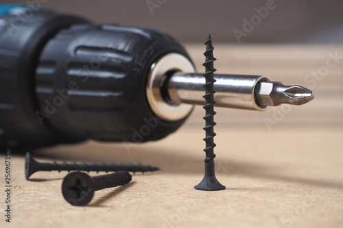 Crosshead screwdriver and self-tapping screws lie on a sheet of fiberboard. Close-up