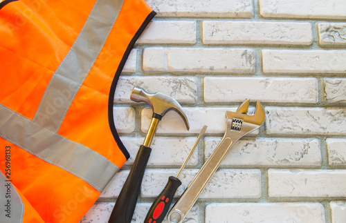 Flat lay composition with protective construction vest and working tool on brick wall background photo