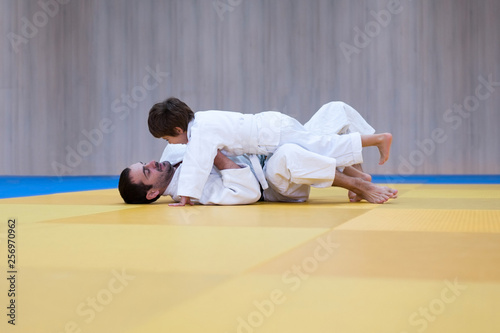 Young judo student and his father engaged in judo class in a dojo. Trainer teaches child the methods and positions of ground fighting in judo or brazilian jujutsu