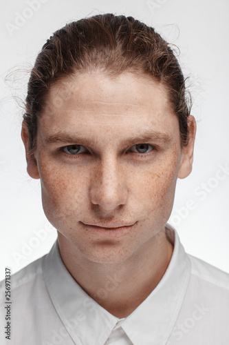 Portrait of a handsome long-haired man with drawn hair and freckles dressed in a white shirt