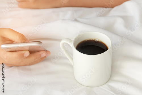 Coffee in bed; Hand holding a cup of black coffee and using mobile phone on bed. Lifestyle and simply perfect morning.