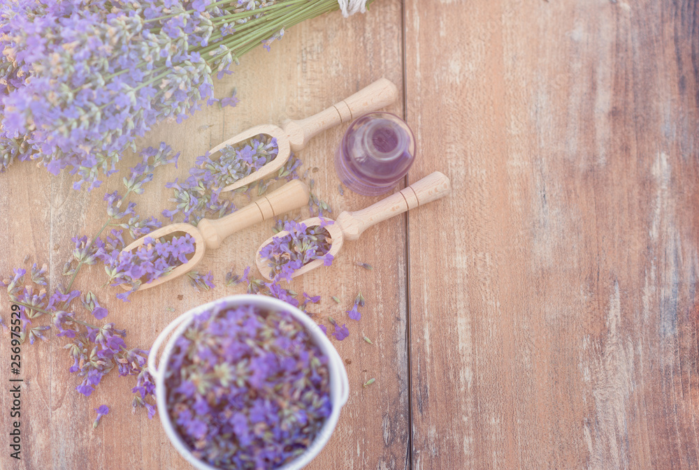 Top view of a bowl and wooden spoons with fresh lavender flowers, lavender essential oil and a bouquet of lavender on a brown wooden background. Top view of a bowl and wooden spoons with fresh lavender flowers, lavender essential oil and a bouquet of lavender on a brown wooden background.