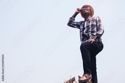 African man photographer Standing holding sunglasses and film camera on the dry tree.
