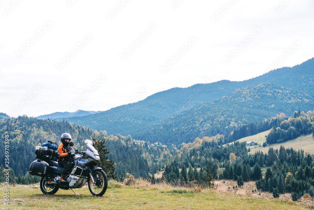 Woman biker with big adventure motorbike, motorcyclists vacation, world traveler, long road trip on two wheels. autumn day. Mountains on background. Romania Woman biker with big adventure motorbike, motorcyclists vacation, world traveler, long road trip on two wheels. autumn day. Mountains on background. Romania