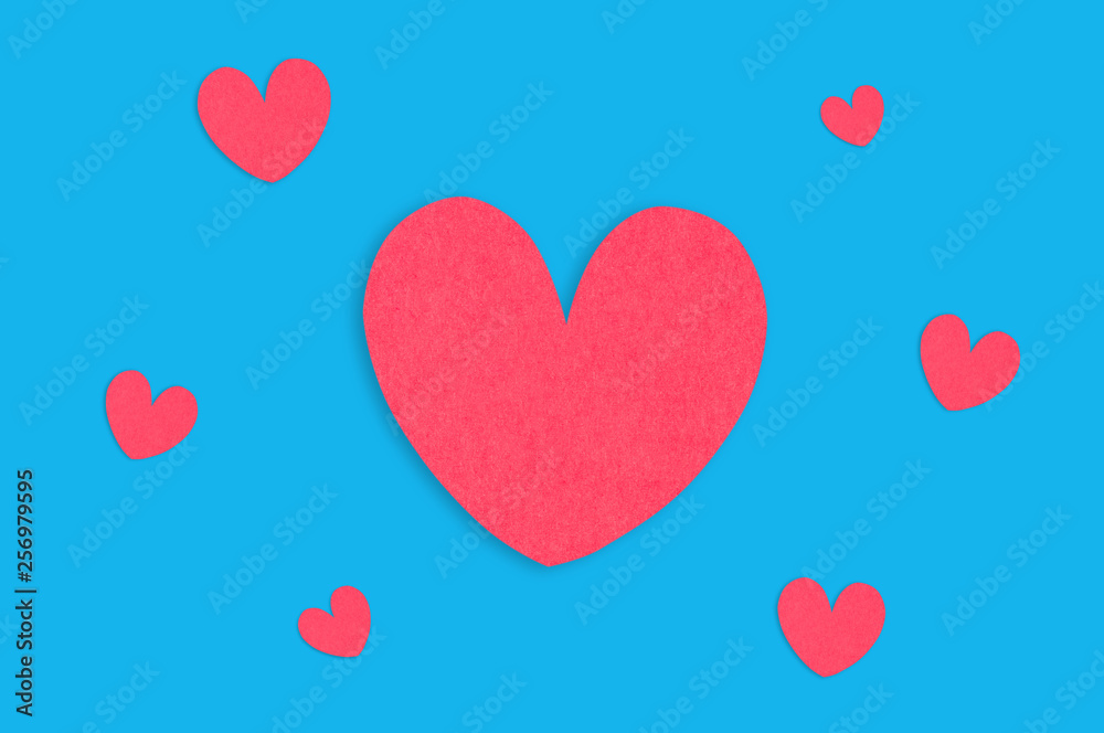 One big red paper heart and scattered small hearts in center of blue table. Top view. Valentines Day concept