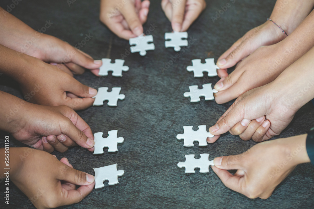 Hands of diverse people assembling jigsaw puzzle, team put pieces together searching for right match, help support in teamwork to find common solution concept, top close up view Hands of diverse people assembling jigsaw puzzle, team put pieces together searching for right match, help support in teamwork to find common solution concept, top close up view
