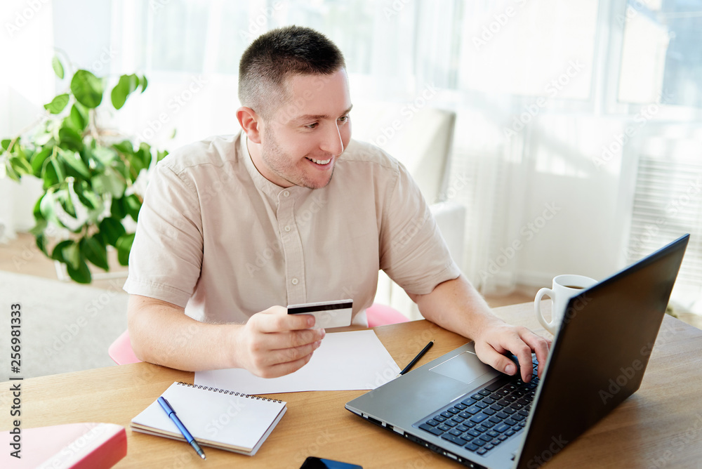 Happy smiling man booking hotel on laptop with credit card at home office, copy space. Technology, banking, paying, online shopping concept Happy smiling man booking hotel on laptop with credit card at home office, copy space. Technology, banking, paying, online shopping concept