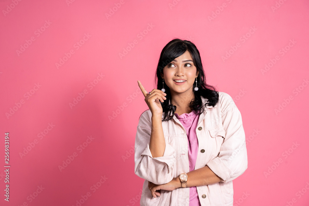 casual young woman thinking and pointing up to copyspace on pink background casual young woman thinking and pointing up to copyspace on pink background