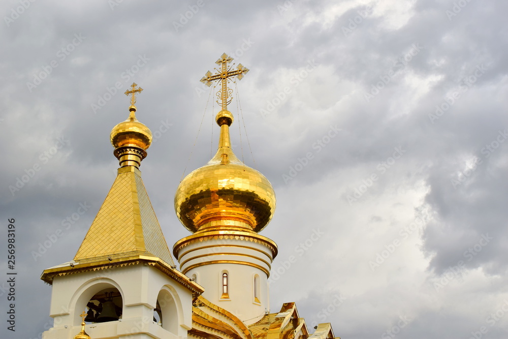 Golden domes of the white сhristian сhurch. White stone walls of the temple. Bright gilt domes. Stormy sky. Close up. Copy space.