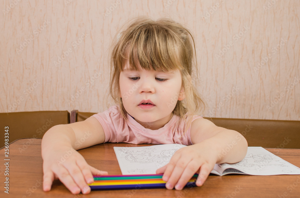 Cute little girl paints and tinkers with colored pencils and scissors Cute little girl paints and tinkers with colored pencils and scissors