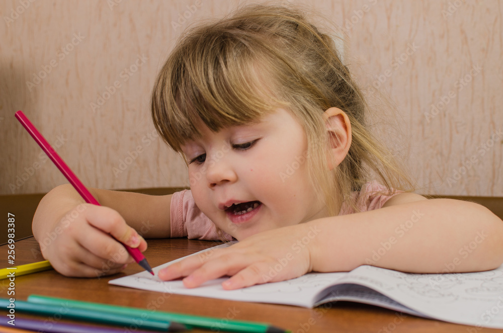 Cute little girl paints and tinkers with colored pencils and scissors Cute little girl paints and tinkers with colored pencils and scissors