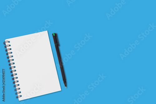 One paper notepad with spiral binder and blank sheets near black plastic pen lies of blue office table. Top view. Copy space for your text. Concept of business or education