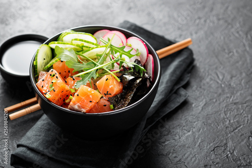 Salmon fish poke bowl with rice, radish,cucumber, tomato, sesame seeds and green onion. photo