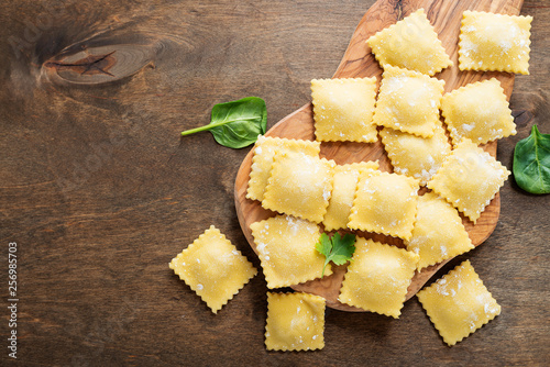 Tasty raw ravioli with flour and greens on dark background. 