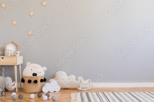 Stylish scandinavian newborn baby room with toys, children's chair, natural basket with teddy bear and small shelf. Modern interior with grey background walls, wooden parquet and stars pattern. photo