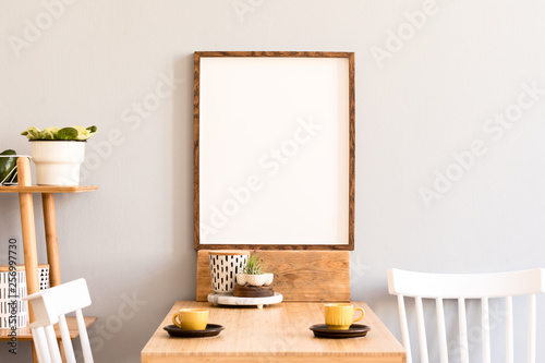 Fototapeta Naklejka Na Ścianę i Meble -  Stylish retro and sunny interior of kitchen space with wooden table with mock up photo frame, design furnitures and yellow cups. Scandinavian room decor with accessories, bamboo shelf and plants.